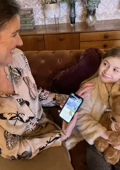 A woman and a child on a sofa looking at memories on a phone, with a teddy bear beside them